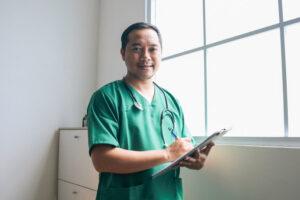 Junger asiatischer Arzt, der lächelnd medizinische Unterlagen im Krankenhaus hält