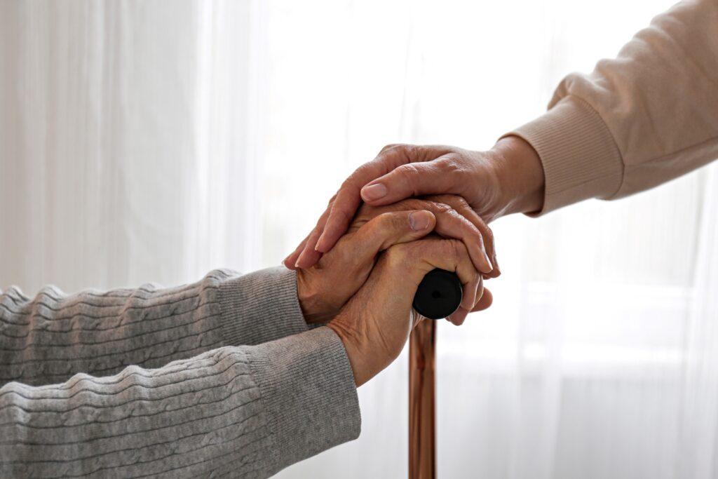 Eine Pflegekraft hält fürsorglich die Hand einer älteren Person mit Gehstock in Münster, symbolisierend die vertrauensvolle und unterstützende Beziehung im Pflegedienst