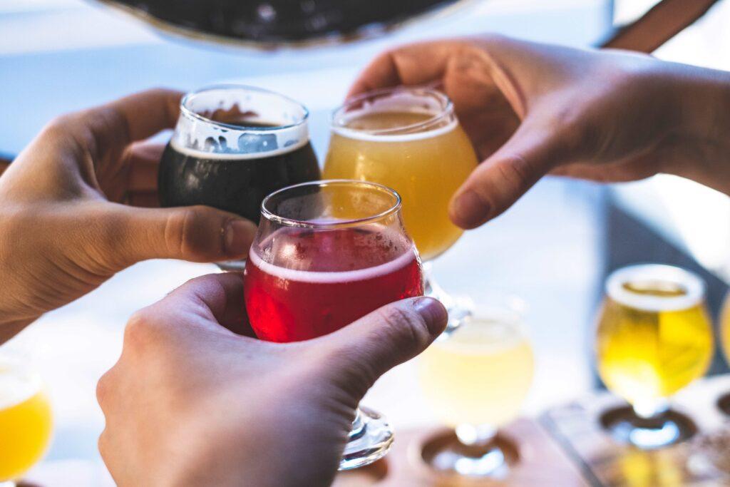 Drei Personen stoßen mit verschiedenen Gläsern belgischen Biers an, jeweils gefüllt mit dunklem, hellem und rotem Bier.